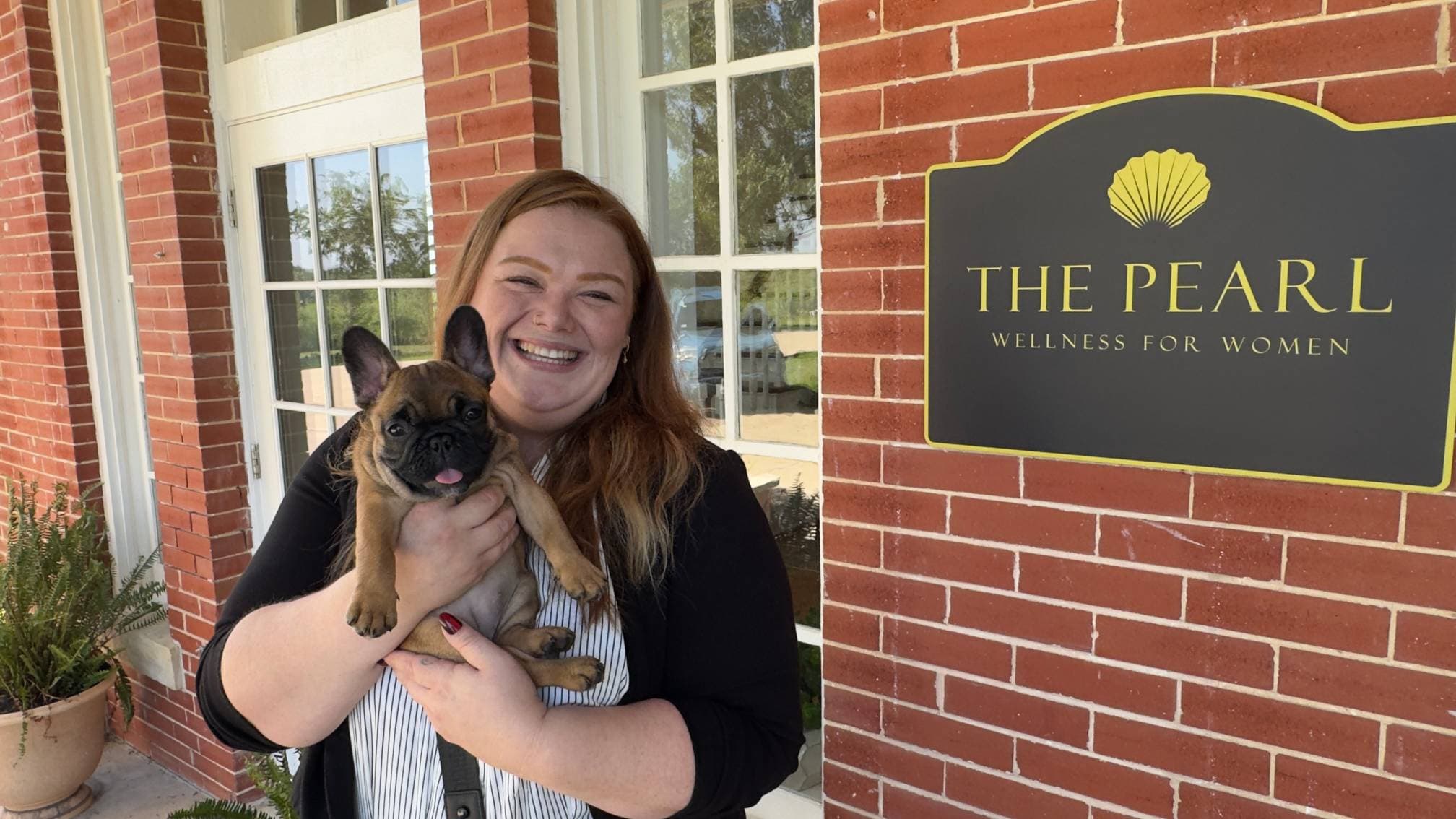 Morgan Gaither bế chú chó bulldog Pháp Bougie trước cơ sở The Pearl Wellness for Women