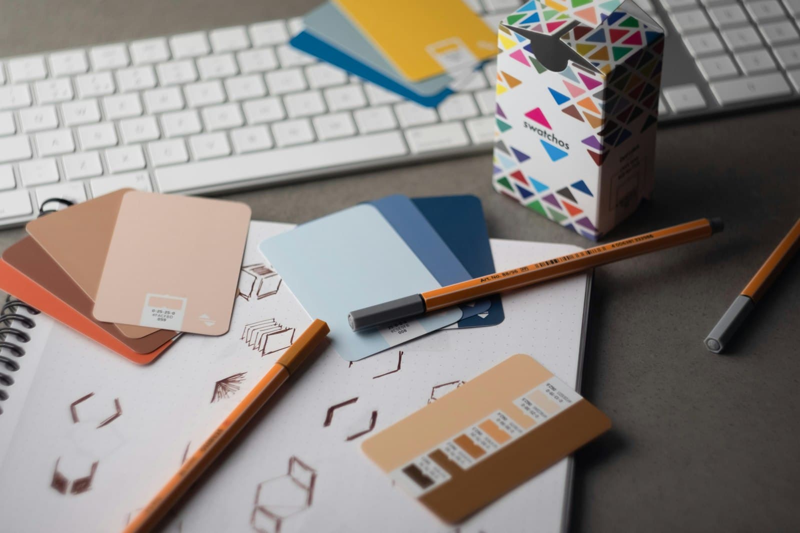 a desk with a keyboard, pencils, and various color samples — Photo by Andy Brown on Unsplash