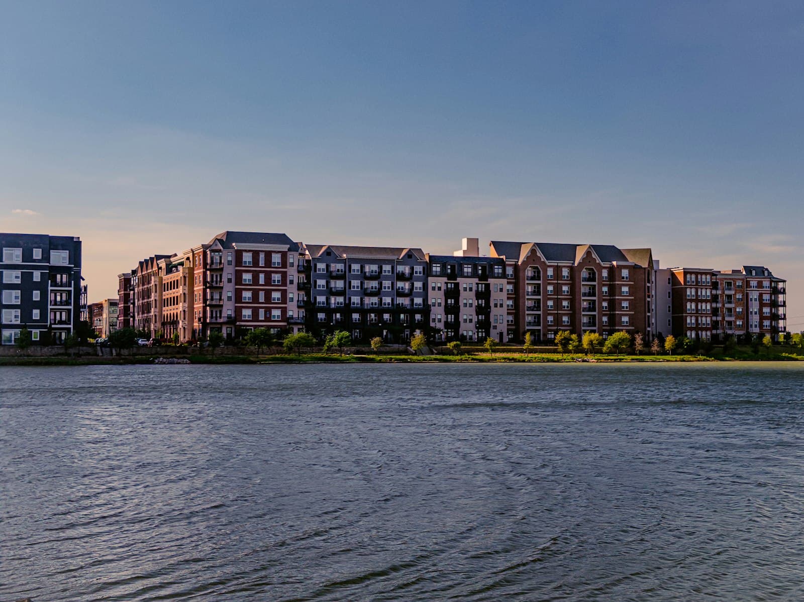 Modern apartment buildings line a waterfront under a clear sky — Photo by Sankalp Mudaliar on Unsplash